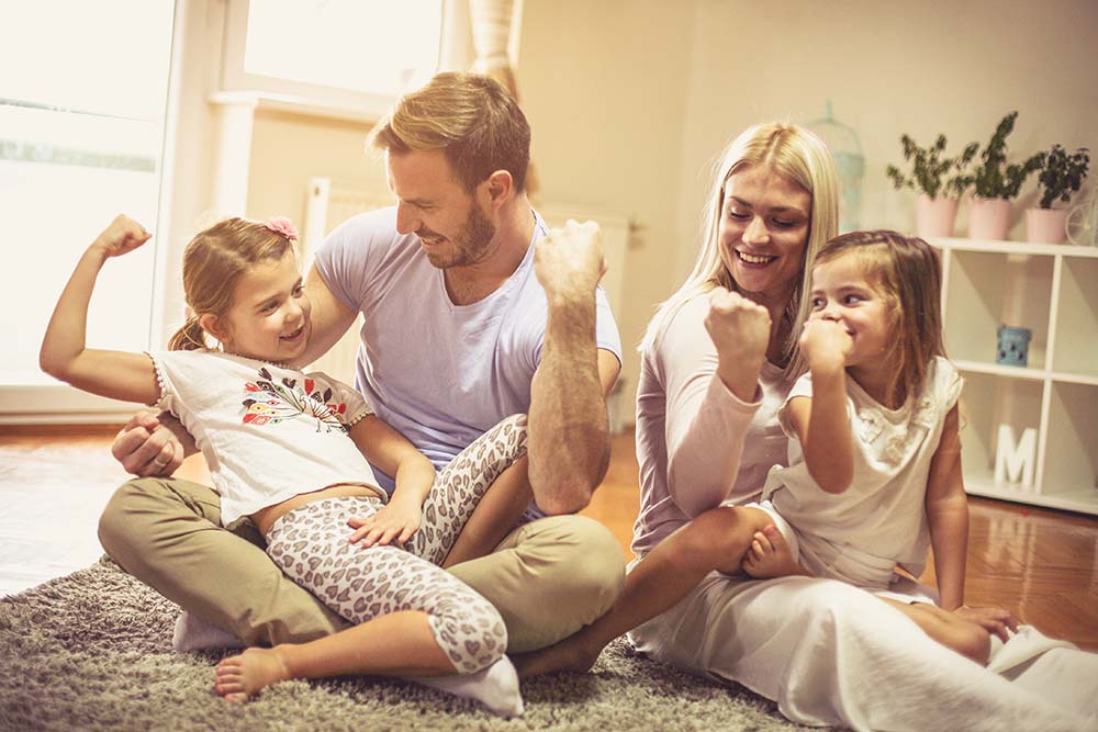 A young family laughing and posing their arms in their living room